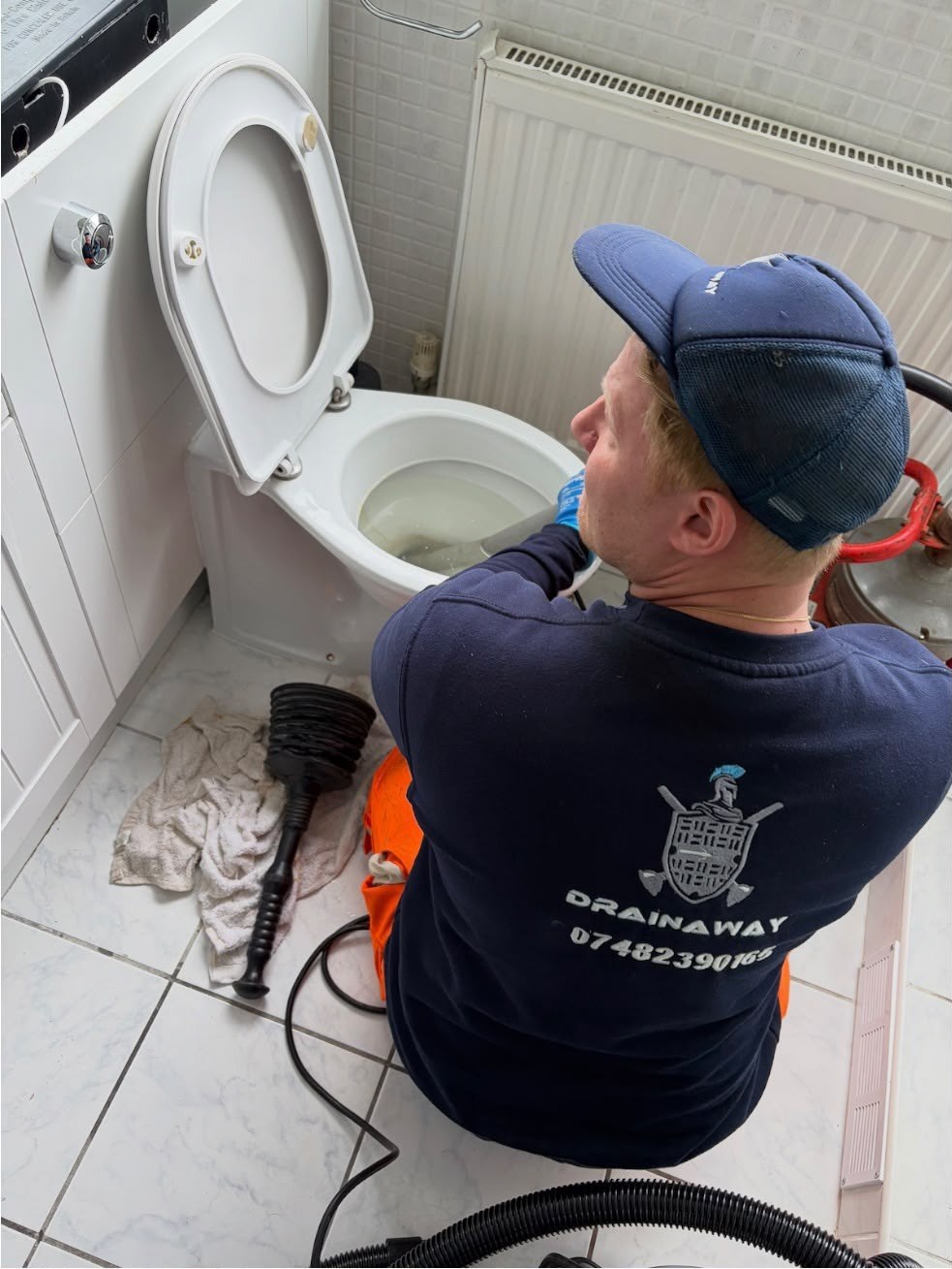 A DrainAway engineer clearing a blocked toilet with a drain machine in a customer's bathroom