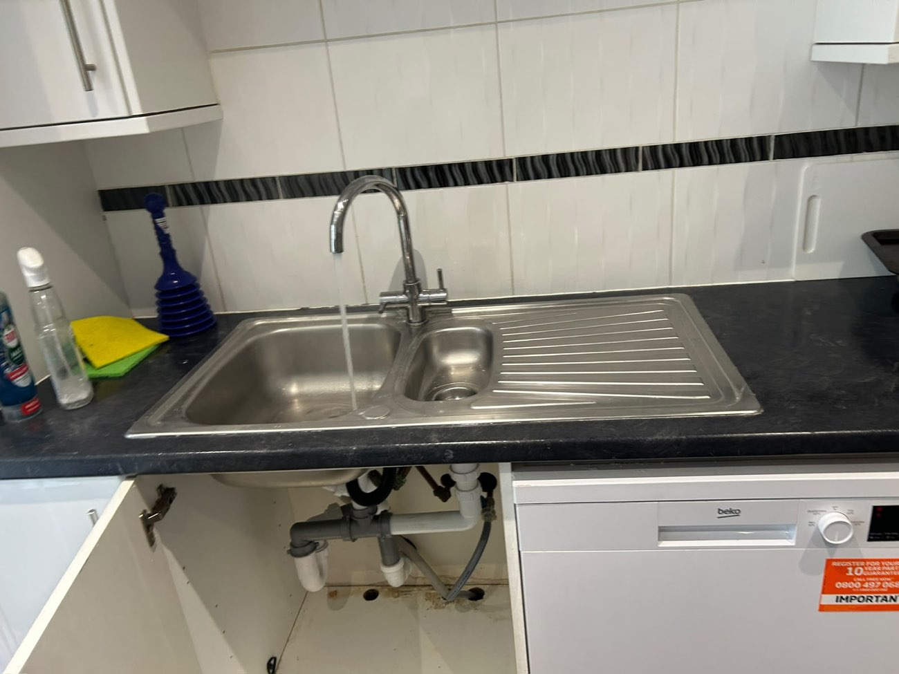 The same kitchen sink clean and empty, with the tap running clear and draining freely.
