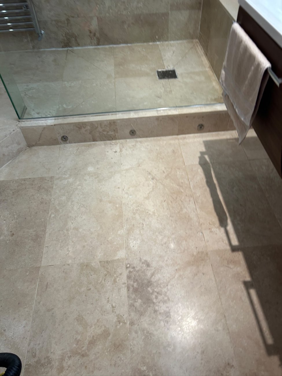 The same travertine wet room floor clean and dry, with the shower drain running clear.