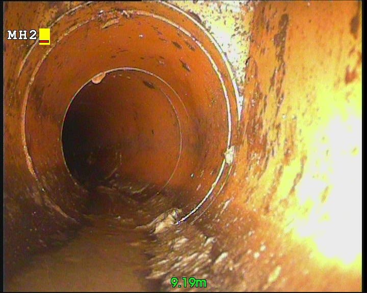 CCTV camera still looking along a clay drain pipe towards a manhole.
