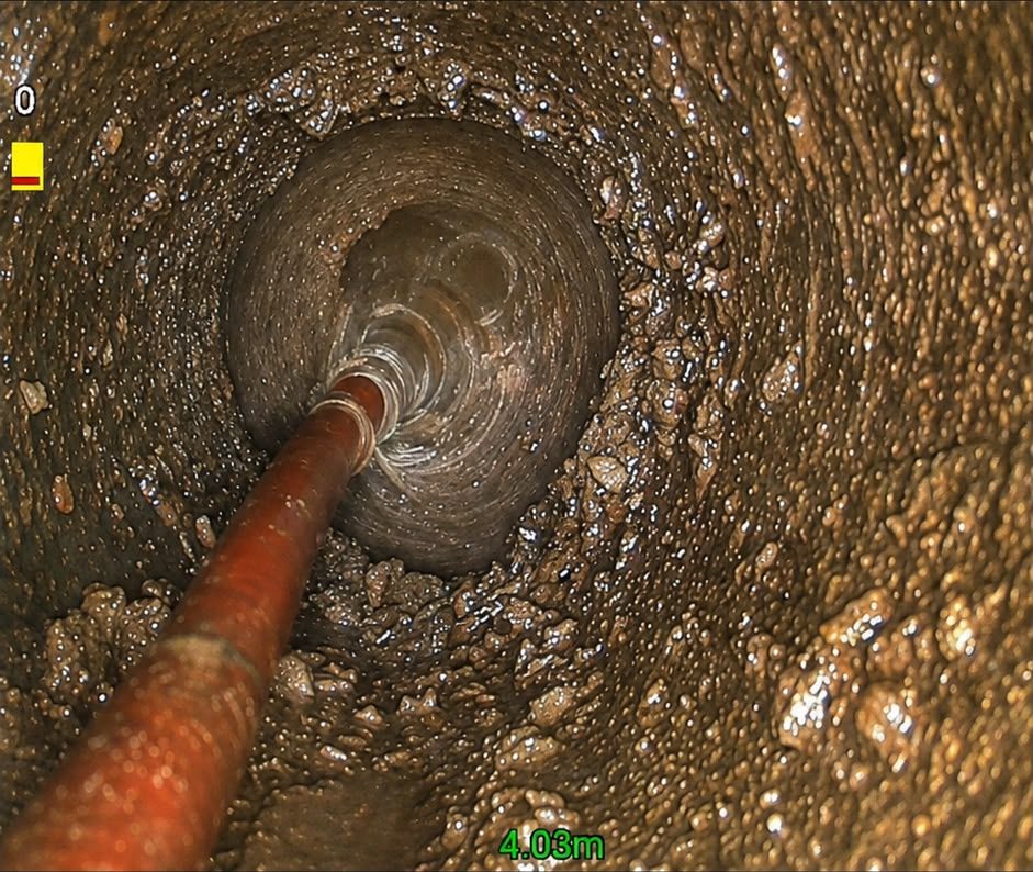CCTV survey still of a jetting hose working along a drain heavily coated in fat and silt build-up.