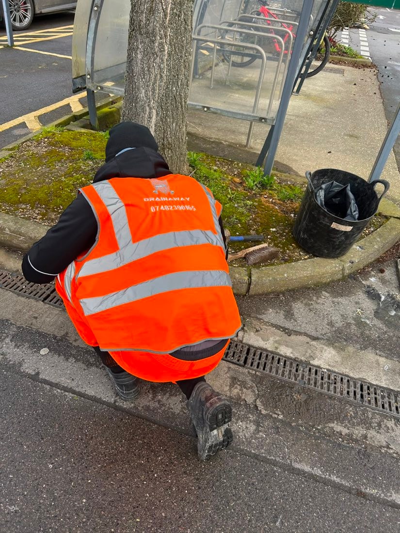 A DrainAway engineer in a high-visibility vest clearing a roadside gully by the kerb.