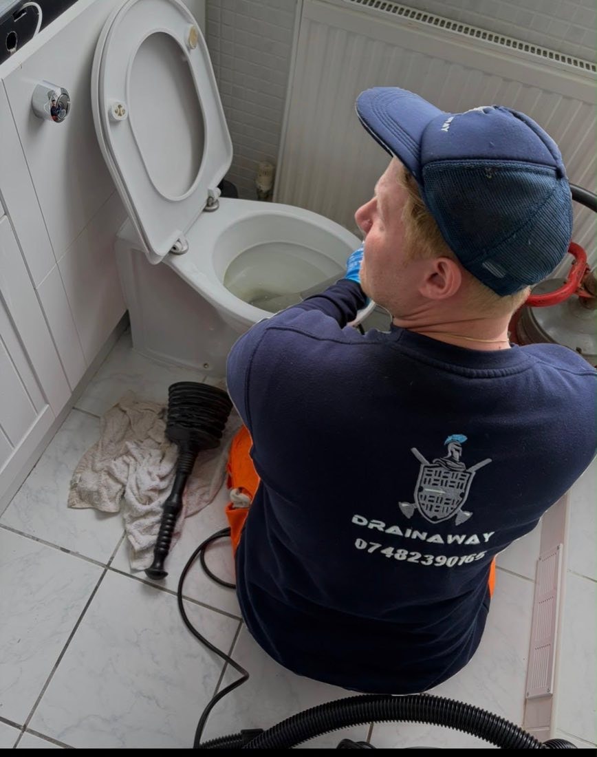A DrainAway engineer in branded uniform clearing a blocked toilet in a domestic bathroom.