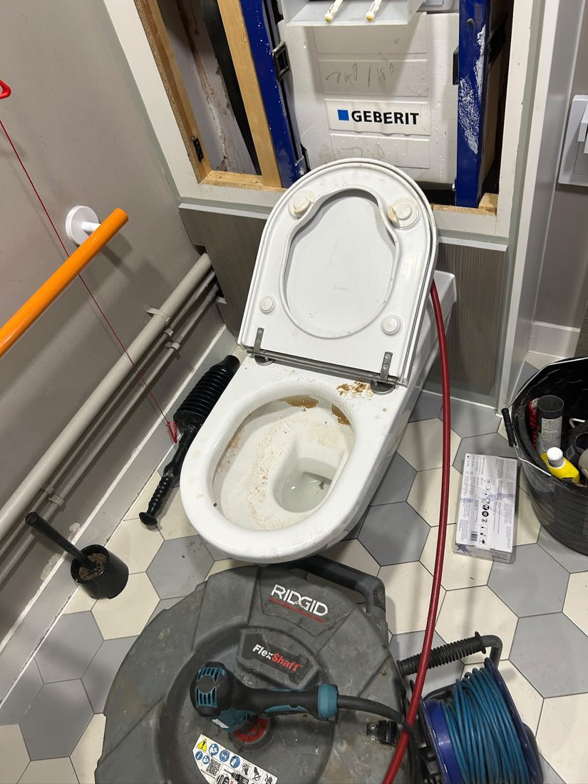Flex shaft machine and hose set up in a commercial toilet cubicle beside a soiled pan.