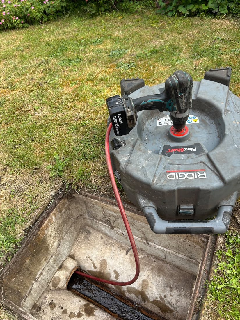 A RIDGID FlexShaft drain machine set up on a lawn beside an open brick inspection chamber.