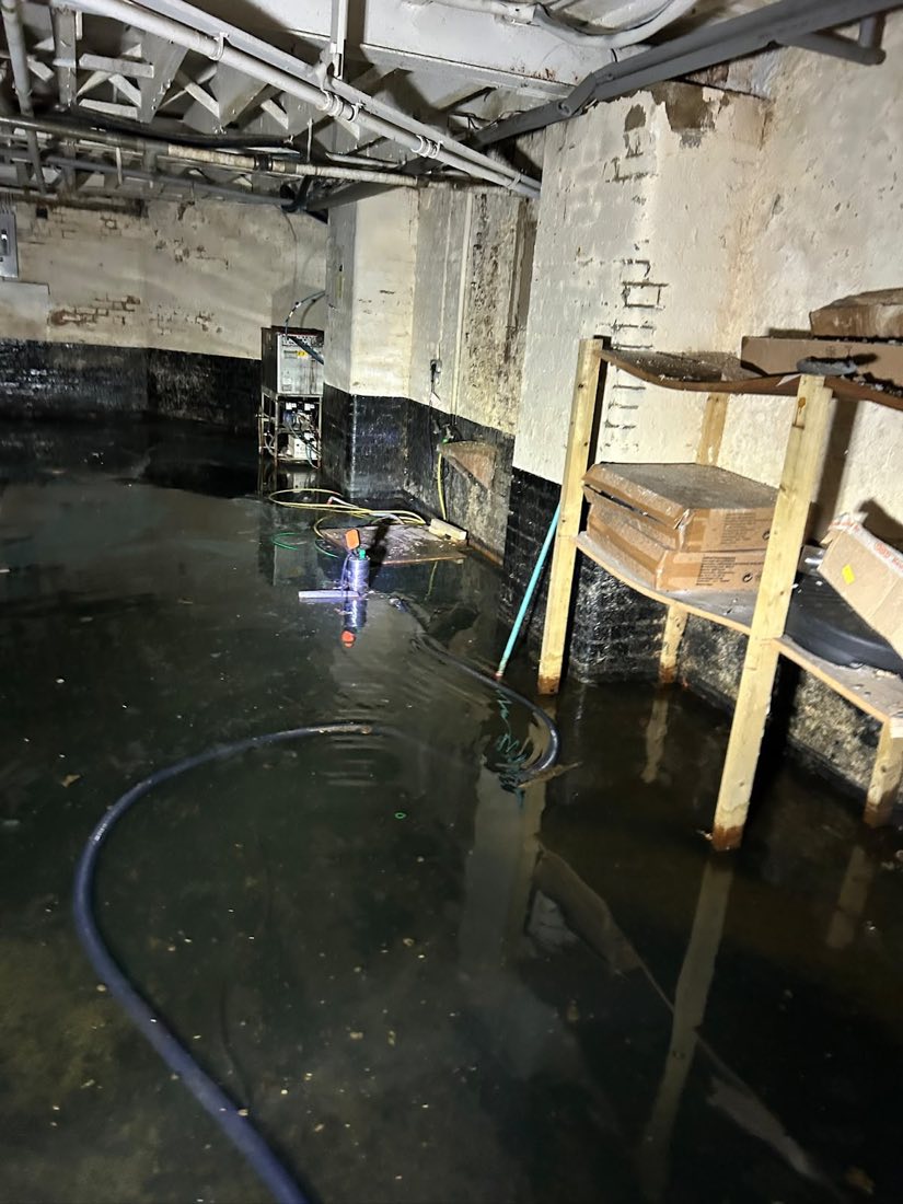 A cellar flooded with standing water, with a pump and hose set up to clear it