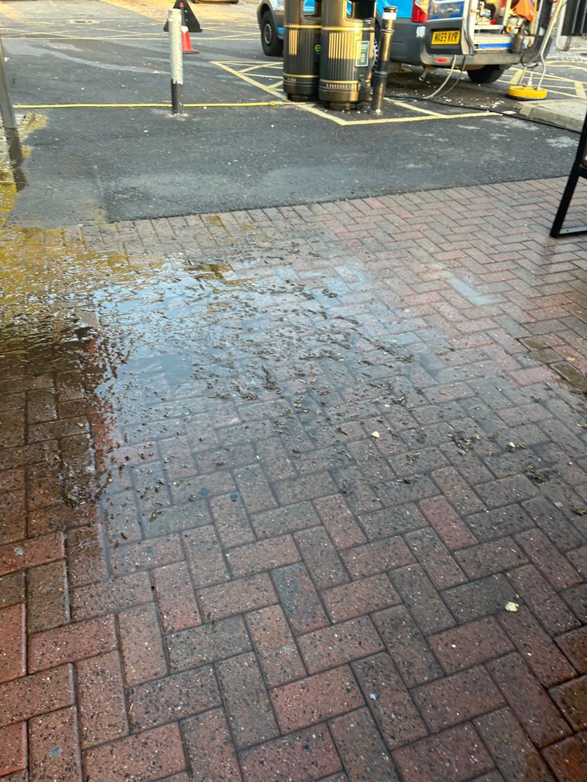 A commercial forecourt flooded with dirty standing water across the block paving.