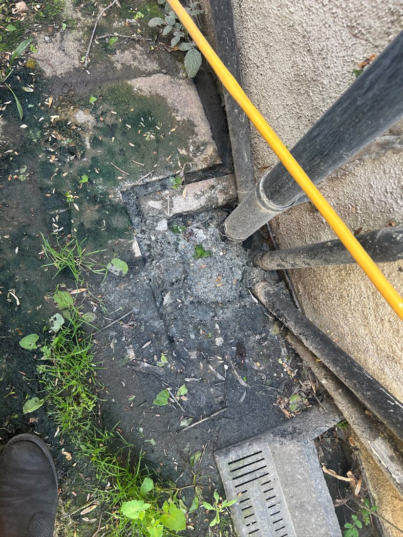 A jetting lance being used to clear a blocked channel drain beside a wall.
