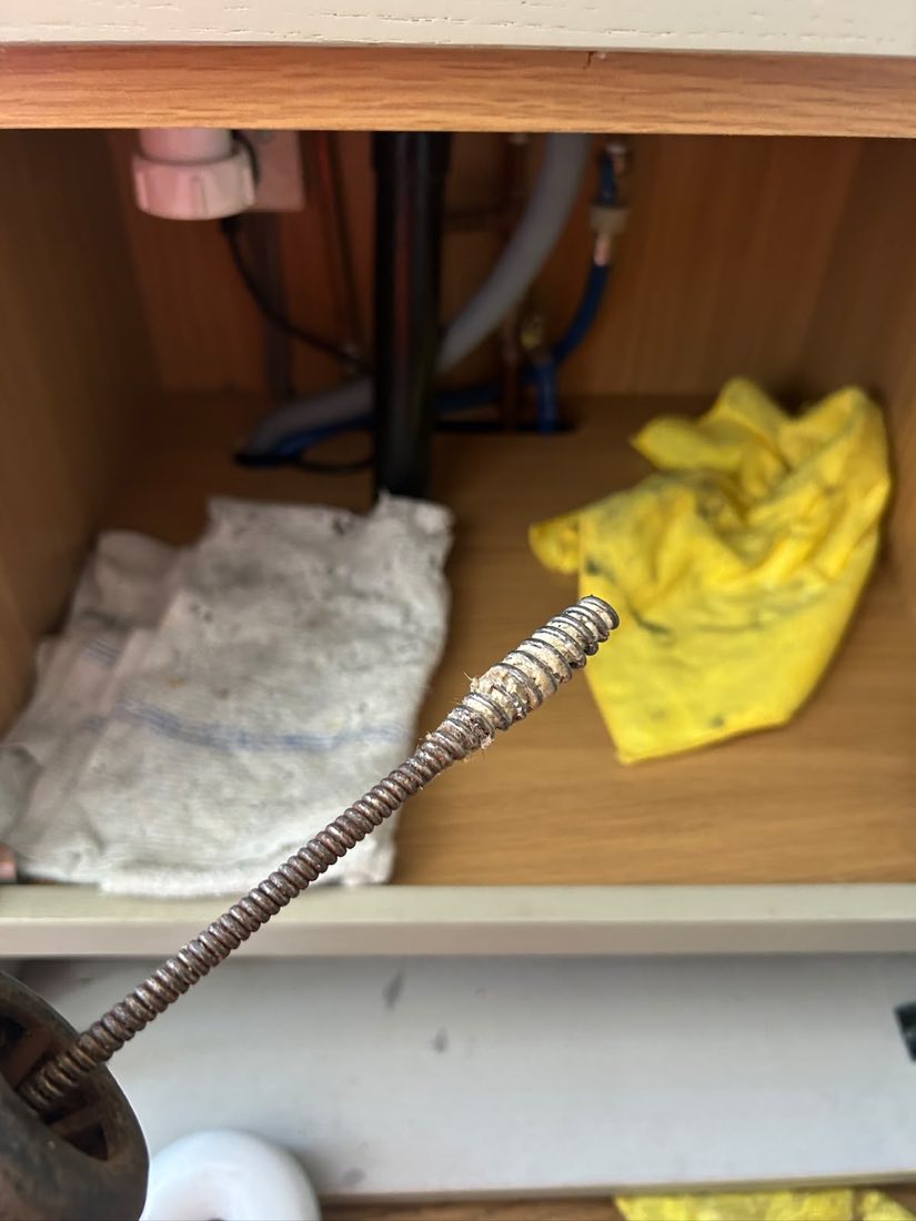A drain rod being fed into waste pipework inside a kitchen cupboard under the sink.