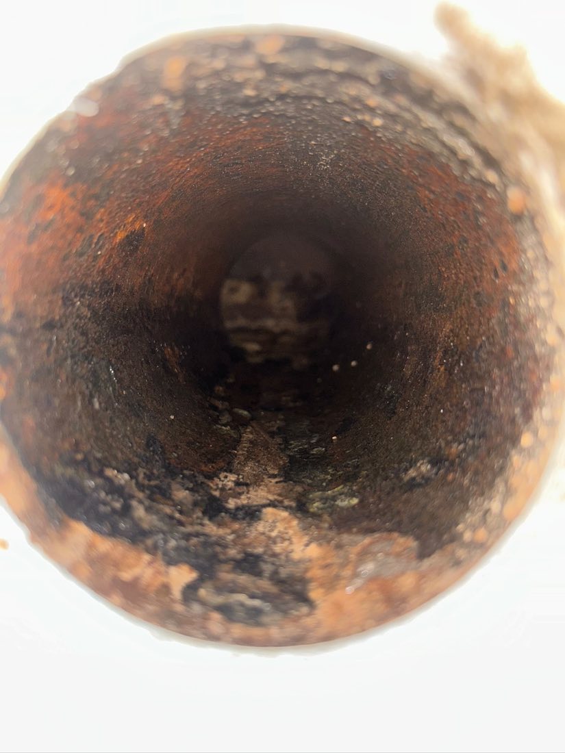 Looking down the inside of a cast iron pipe heavily coated in hard black and brown scale.