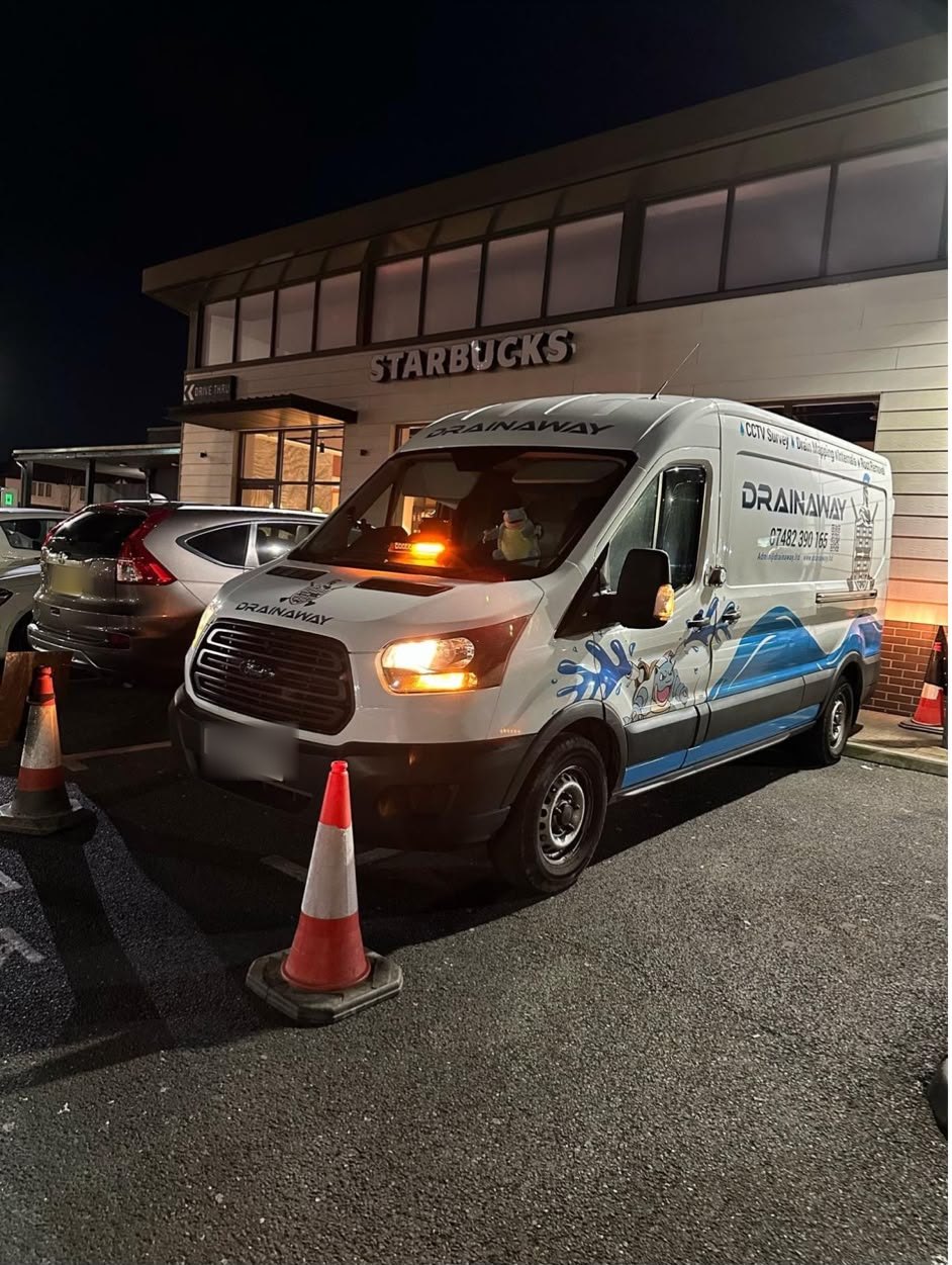 A DrainAway van coned off outside a Starbucks drive-thru at night, on site for a scheduled visit