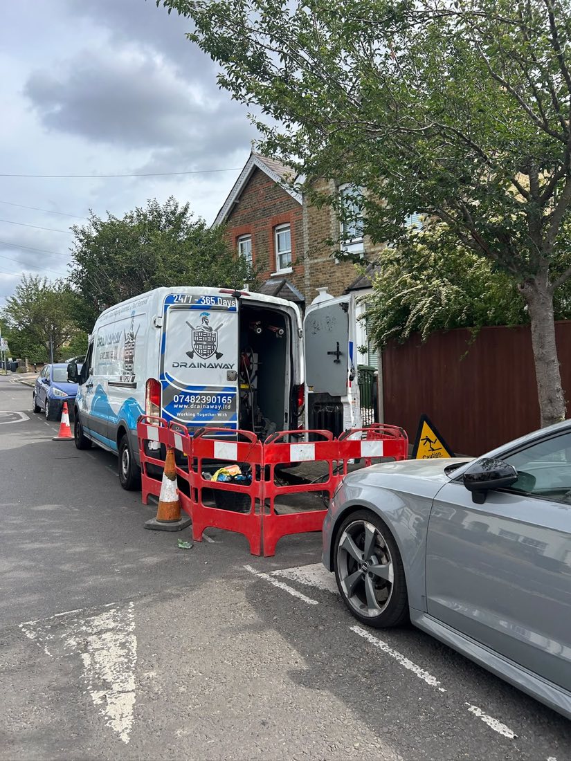 A DrainAway van with its rear doors open and barriers set out on a residential street.