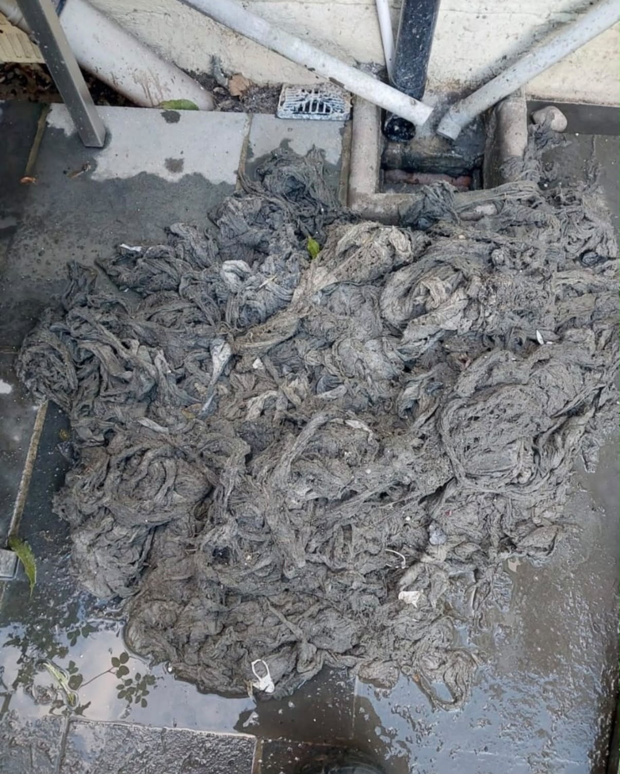 A large mass of wet wipes pulled out of an outside drain and laid on the paving beside the open gully and chamber